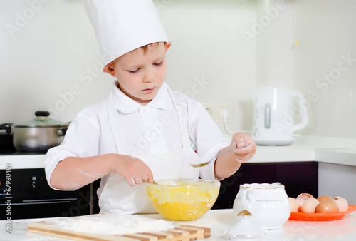 Little boy in chefs uniform baking in the kitchen
