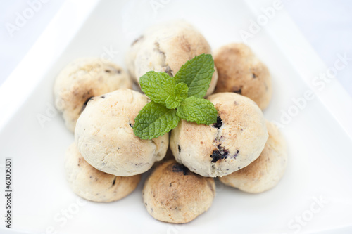 Handmade blueberry cookies with mint on top and in a white bowl on a white background.