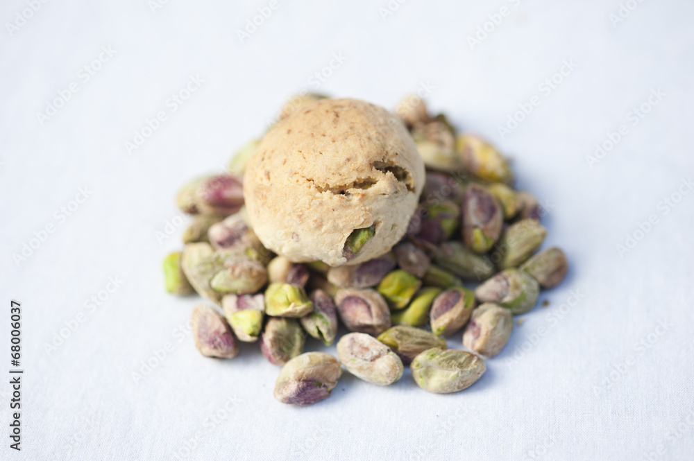 A handmade pistachio cookie on a pile of fresh pistachios on a white background. A handmade pistachio cookie on a pile of fresh pistachios on a white background.