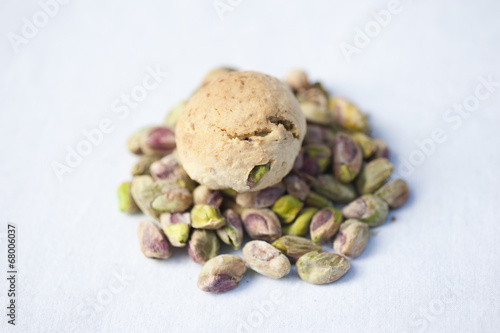 A handmade pistachio cookie on a pile of fresh pistachios on a white background.