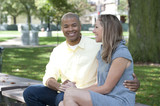 A happy young interracial couple sitting on a bench on a sunny day.