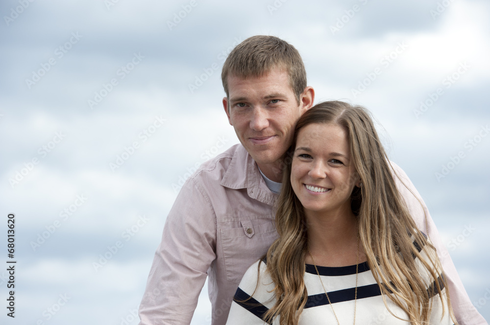A young happy caucasian couple on a sunny day with the clouds in the background at the pier. A young happy caucasian couple on a sunny day with the clouds in the background at the pier.