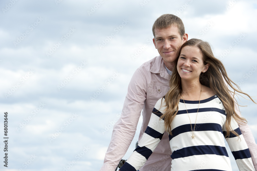 A young happy caucasian couple on a sunny day with the clouds in the background at the pier. A young happy caucasian couple on a sunny day with the clouds in the background at the pier.