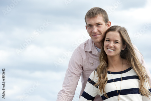 A young happy caucasian couple on a sunny day with the clouds in the background at the pier.