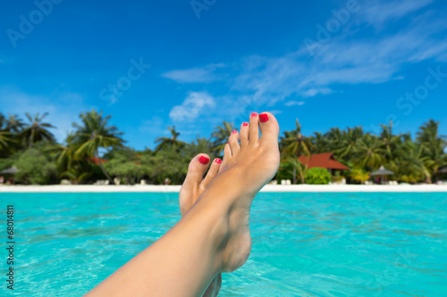 Close-up of female foot in the blue water on the tropical beach.