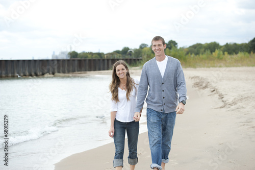 A beautiful happy young caucasian couple smiling and walking barefoot on the beach.