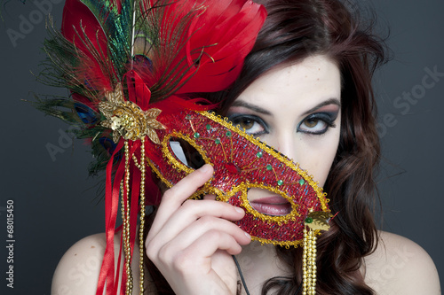 A young attractive model hiding behind a mask and feathers.