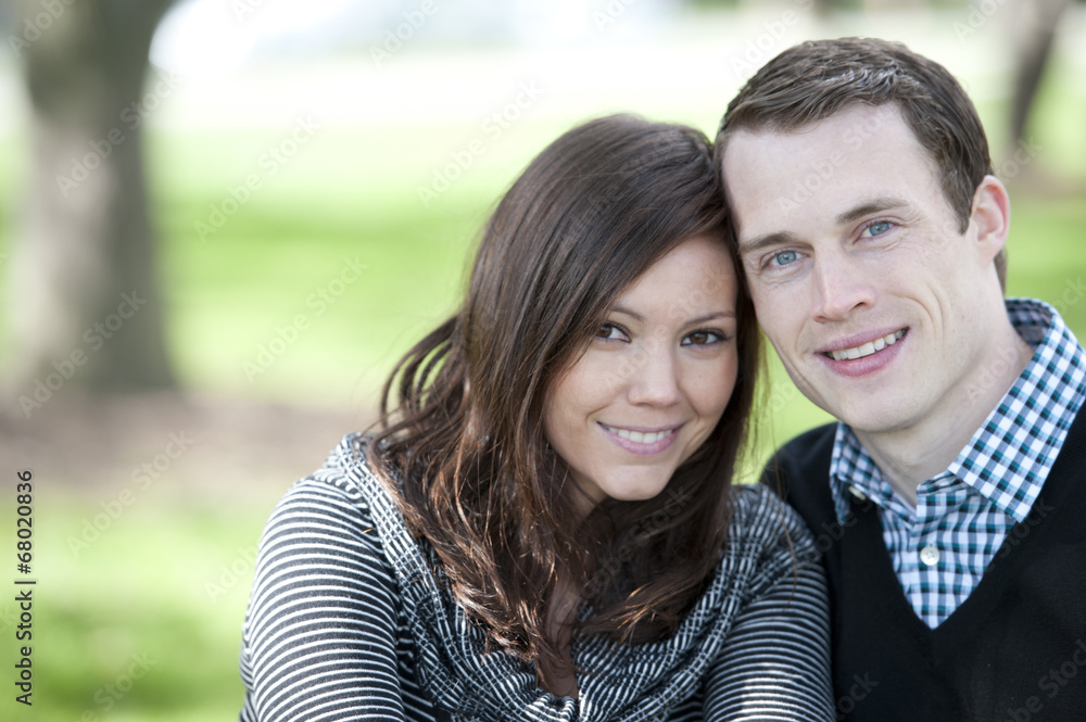 A happy, young and attractive couple looking at the camera on a sunny day at a park A happy, young and attractive couple looking at the camera on a sunny day at a park