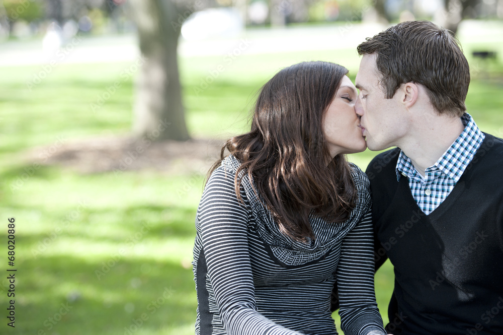 Obraz premium A romantic couple kissing on a sunny day in the park.