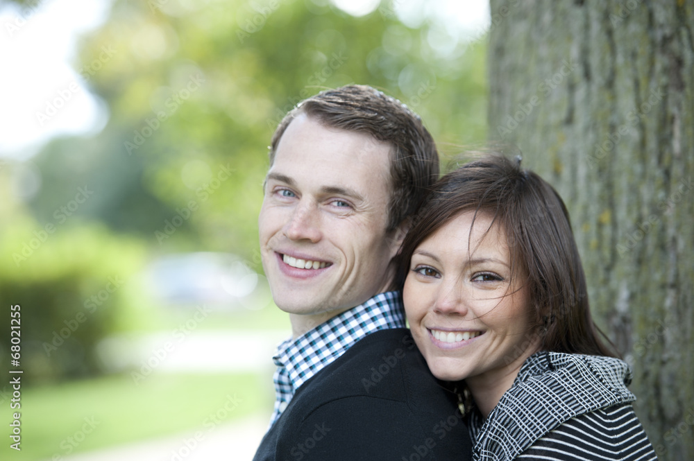 A happy, young and attractive couple looking at the camera on a sunny day at a park A happy, young and attractive couple looking at the camera on a sunny day at a park