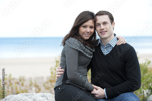 A young and happy couple posing with a beach in the background. © EugeneF