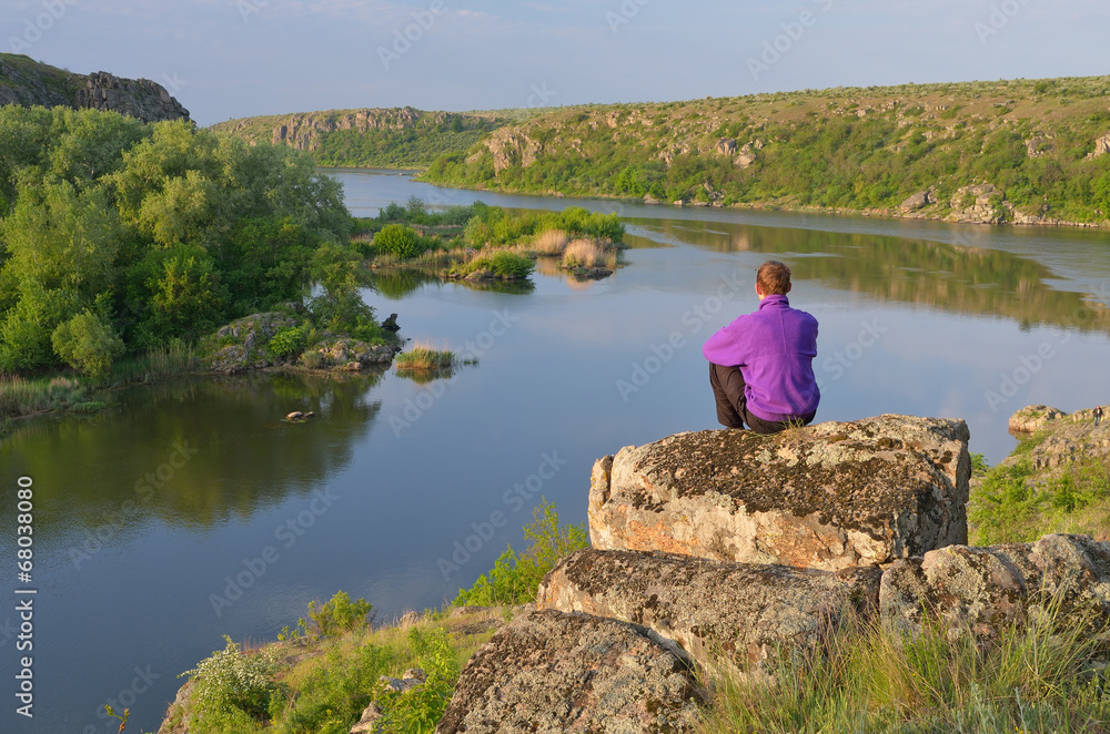 Fototapeta premium Man sits on a rock above the river