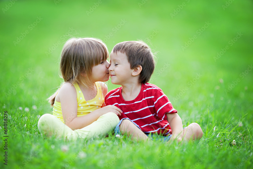 Adorable boy and girl, sitting in the park, smiling and having f Adorable boy and girl, sitting in the park, smiling and having f