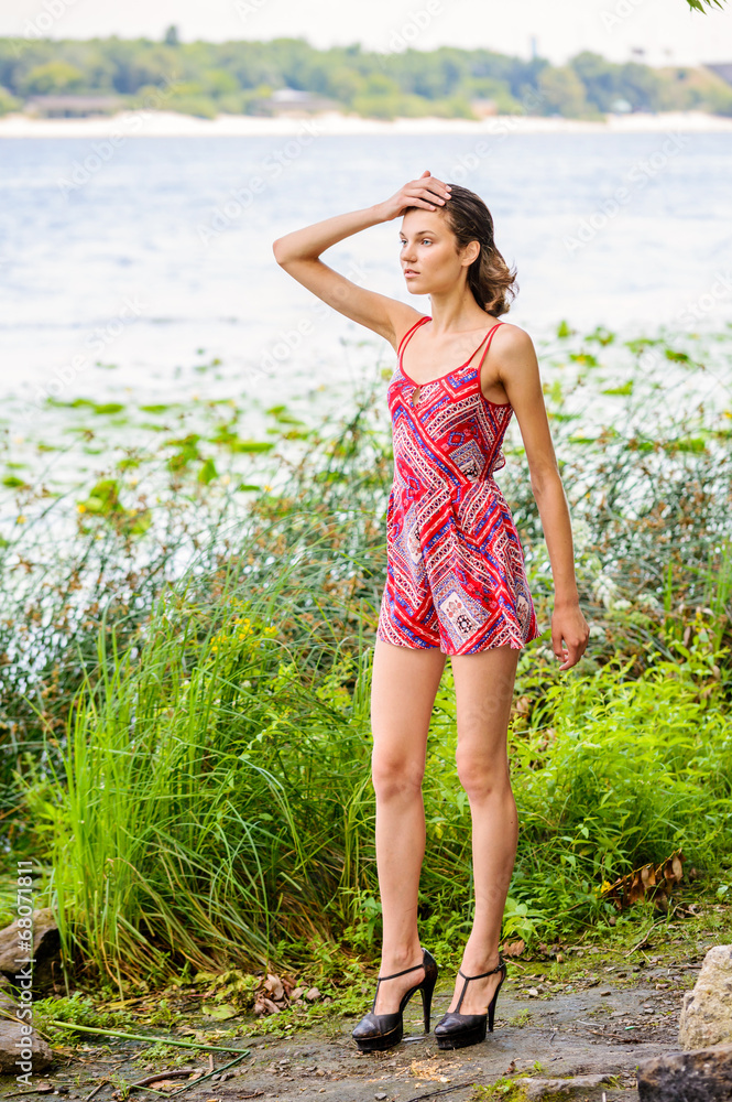 A young woman with a red dress stand close to the river's edge where grow herbs and reeds A young woman with a red dress stand close to the river's edge where grow herbs and reeds