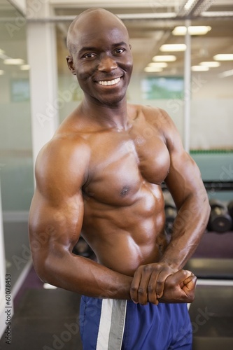 Smiling shirtless muscular man posing in gym