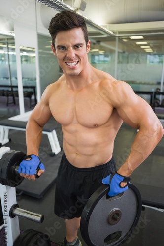 Shirtless young muscular man lifting weight in gym