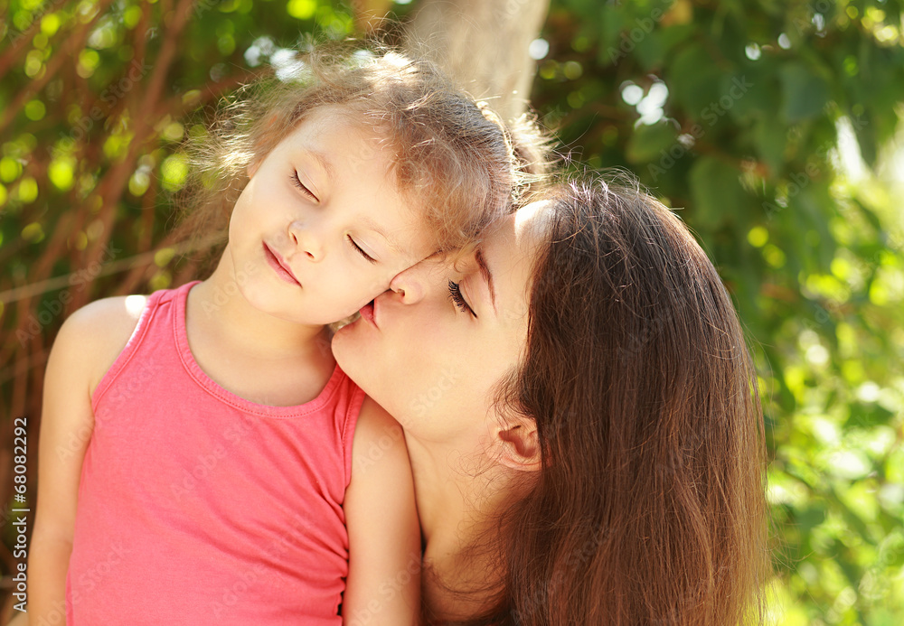 Happy young mother kissing her happy joying kid with love Happy young mother kissing her happy joying kid with love
