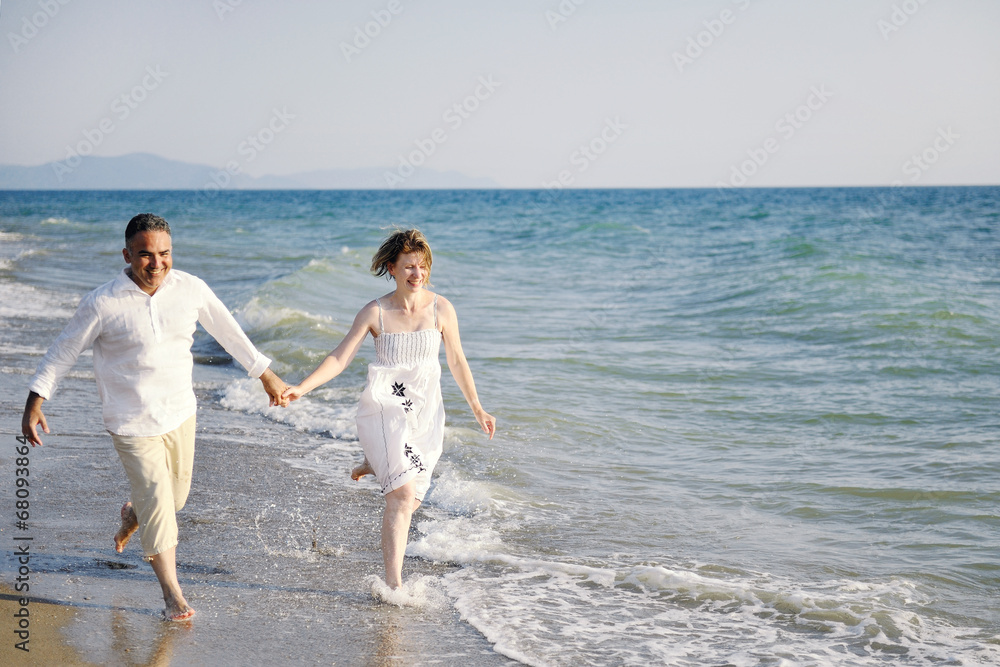 happy couple running through sea waves on the beach