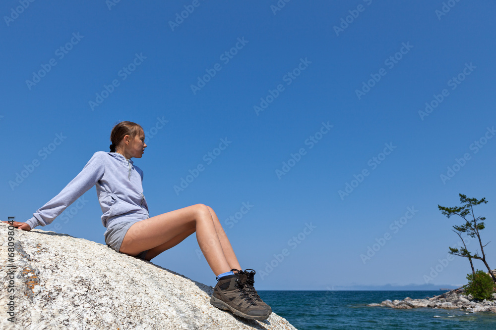 Young woman on big rock against blue sky