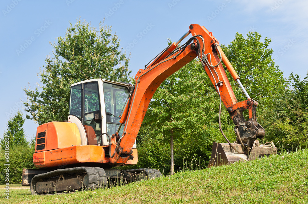Ein Minibagger mit Raupenfahrwerk im Grünen unter blauem Himmel Ein Minibagger mit Raupenfahrwerk im Grünen unter blauem Himmel