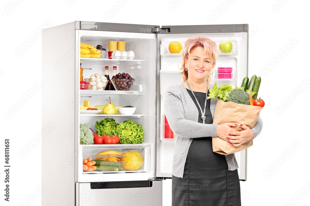 Woman with bag of vegetables in front of a fridge Woman with bag of vegetables in front of a fridge