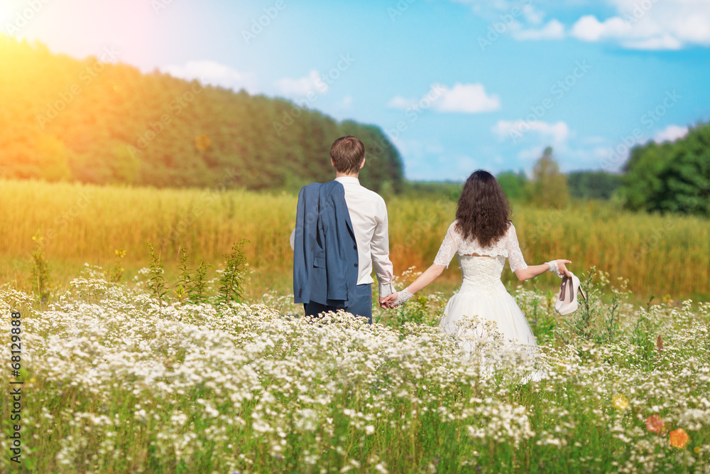 Young happy wedding couple walking in the field and holding hand