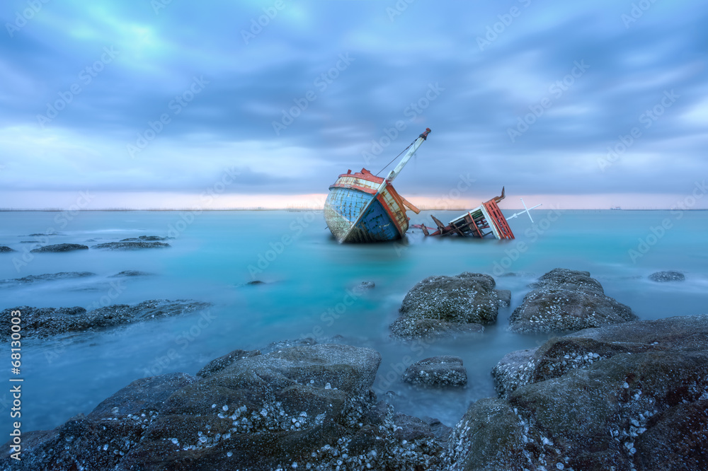 Shipwreck or wood ship broken damage on land, coast or beach with sea and sunset background. That result of accident, storm, crash, wave in ocean or marine. For assurance, travel or adventure concept.