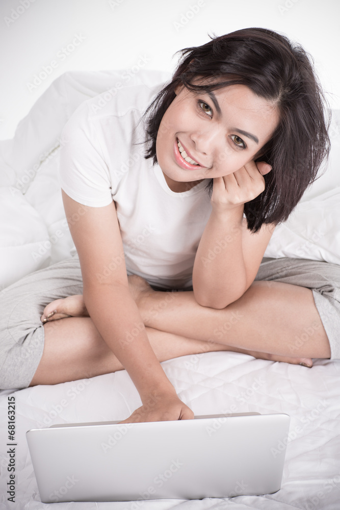 Smiling woman using a laptop while lying on her bed Smiling woman using a laptop while lying on her bed