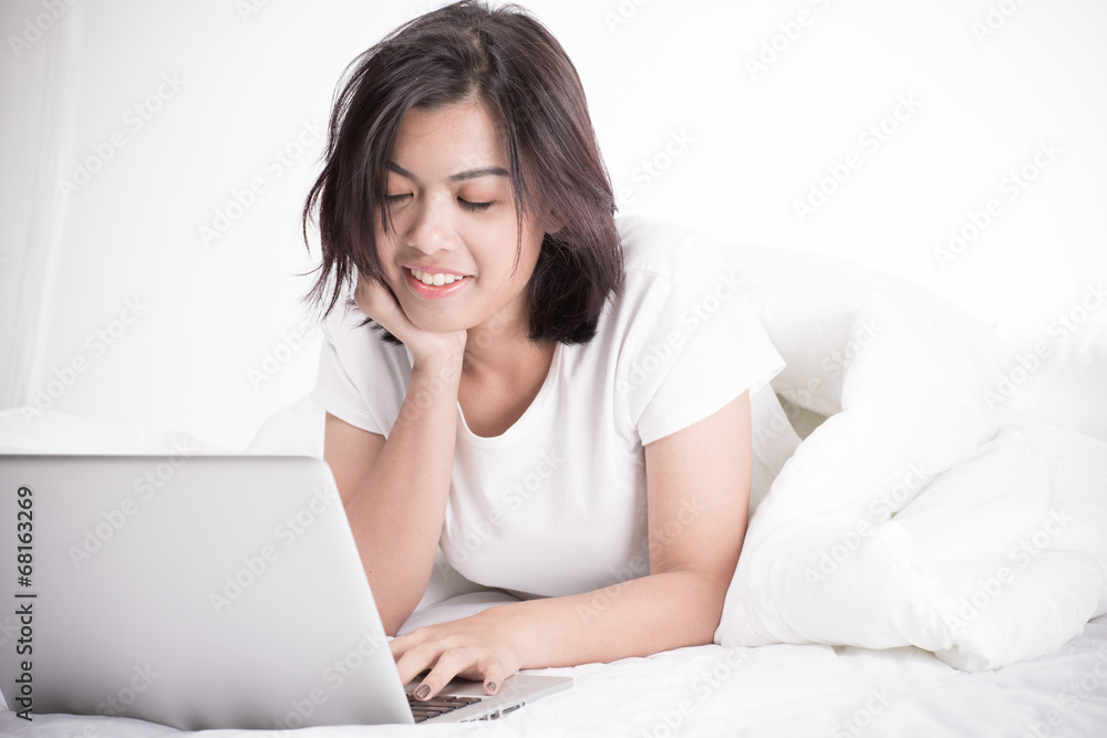 Smiling woman using a laptop while lying on her bed Smiling woman using a laptop while lying on her bed