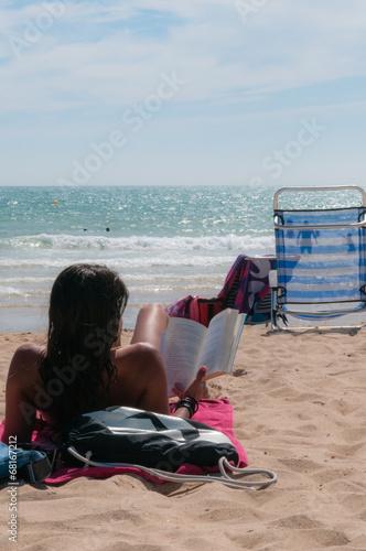 Chica tumbada en la playa leyendo