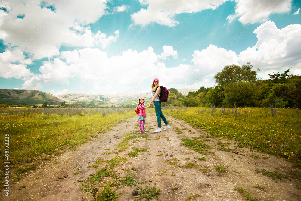 Mother and daughter walk on road through field