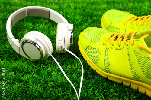 Sport shoes and headphones on green grass background