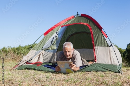 Happy camper looking at map lying in his tent