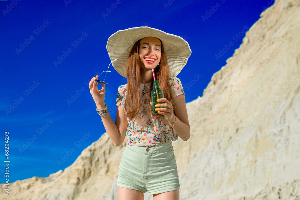Young woman drinking from the bottle on the sky background