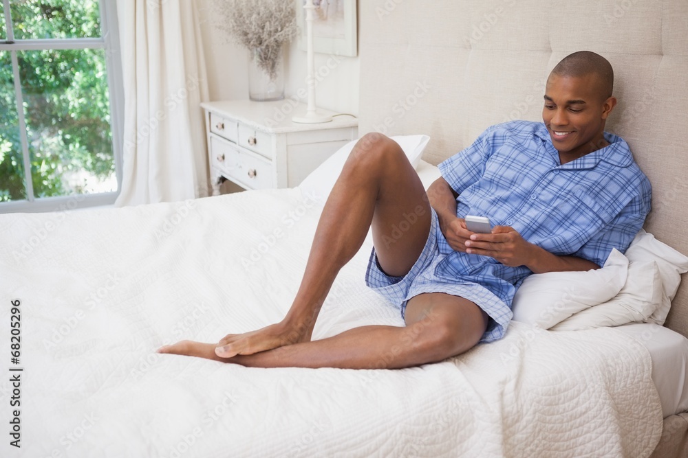 Happy man sitting on bed sending text Happy man sitting on bed sending text