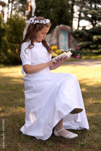 Dziewczynka w białej sukni czyta książeczkę.