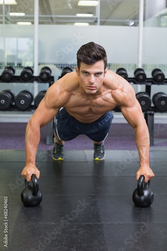 Fototapeta Naklejka Na Ścianę i Meble -  Muscular man doing push ups with kettle bells in gym