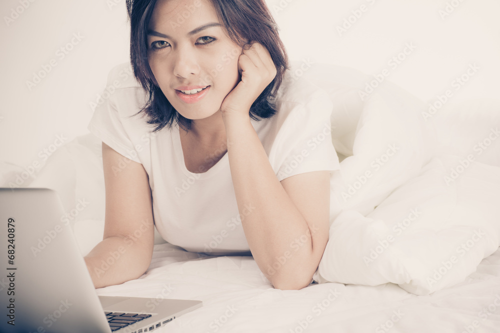 Smiling woman using a laptop while lying on her bed Smiling woman using a laptop while lying on her bed