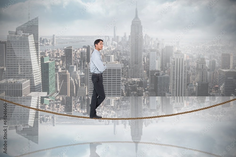 Composite image of serious asian businessman  on tightrope
