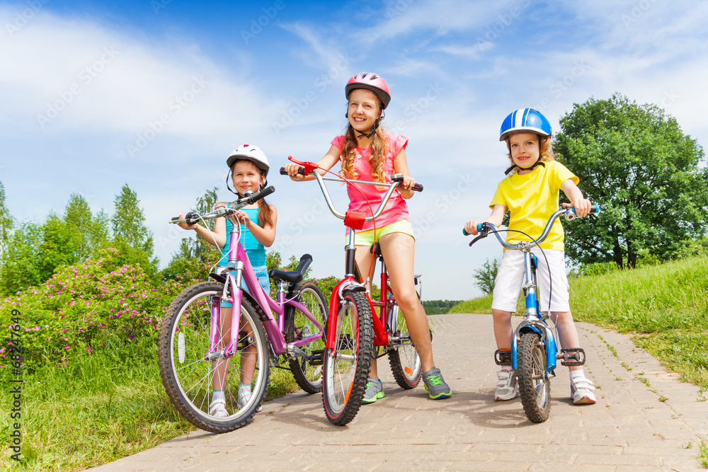 Fototapeta premium Three girls on a pave road with bicycles