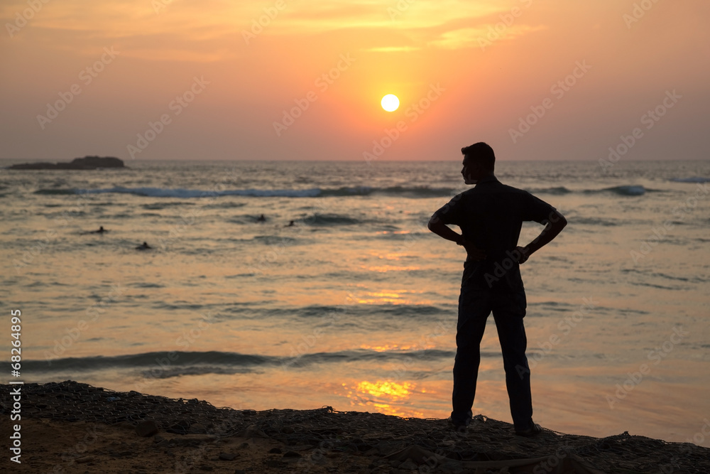 Silhouette  of a man standing on sandy beach at sunset.