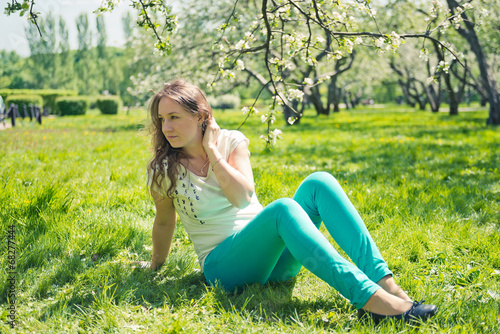 Beautiful girl in green jeans sits on green grass.