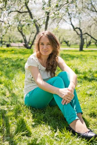 Beautiful  girl in green jeans sits on green grass.