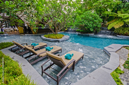 Poolside relax chairs in garden style swimming pool