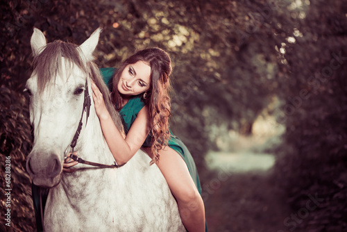 lovely young woman on a white horse at forest path