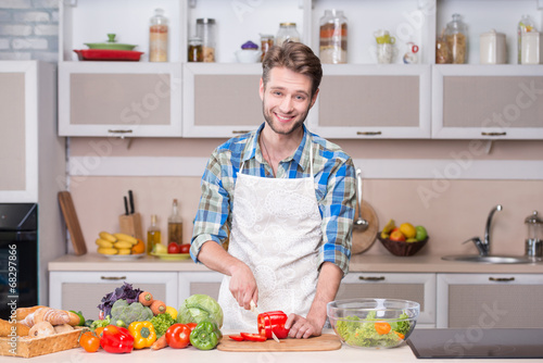 Young smiling man cooking dinner in kitchen