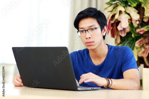 Serious asian man sitting at the table and using laptop
