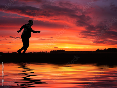 Silhouette of funny overweight man jogging by the lake