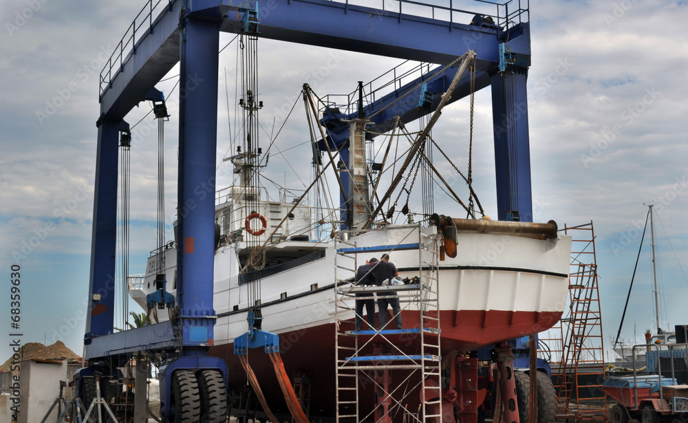 Operai riparano peschereccio in cantiere navale Operai riparano peschereccio in cantiere navale
