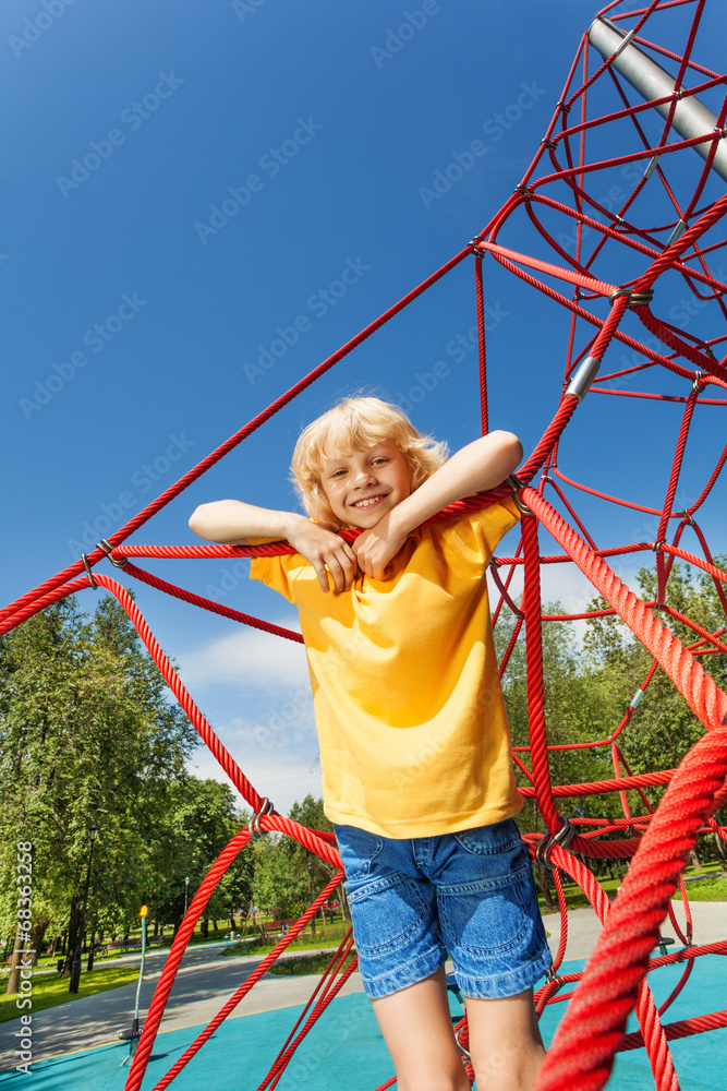 Boy stands on red ropes of net in the park Boy stands on red ropes of net in the park